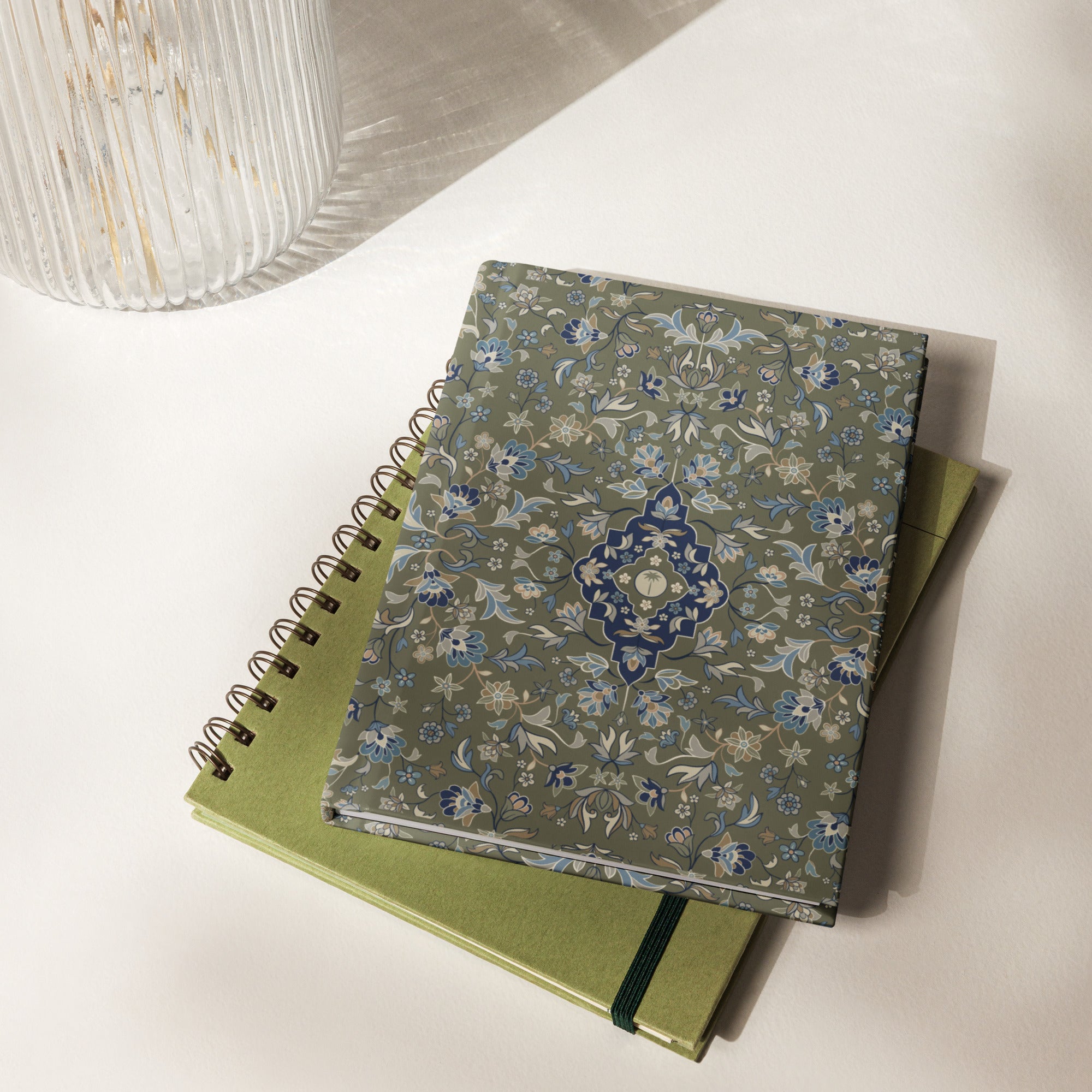 Haramain hardcover matte journal islamic gift resting on a table beside a green spiral notebook.